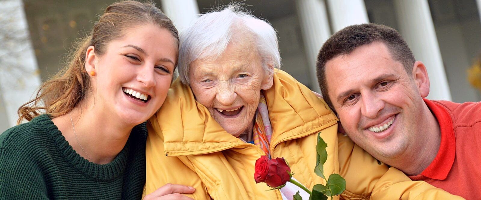 Eine Seniorin lacht gemeinsam mit einer Angehörigen und einem Fahrer von MTK
